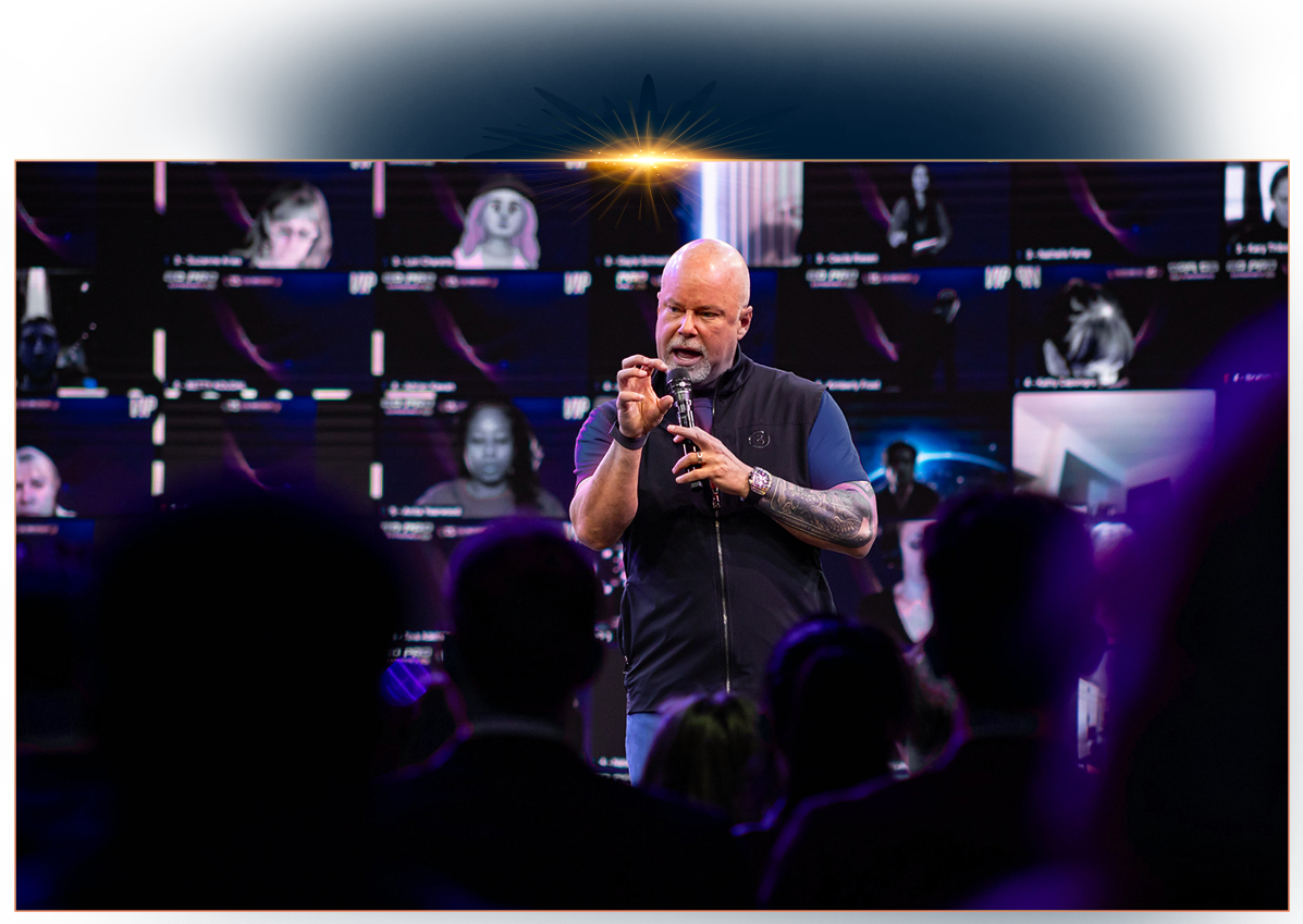 Eric Worre standing in front of a large digital wall of video participants, gesturing with his hands while wearing a dark vest.